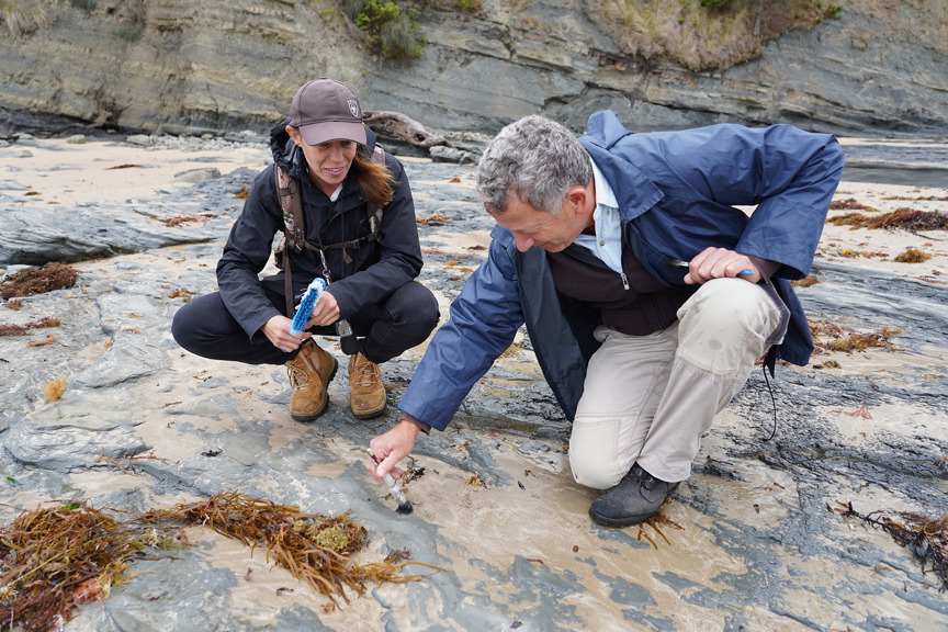 two people crouched on a rocky beach, looking at rock formations
