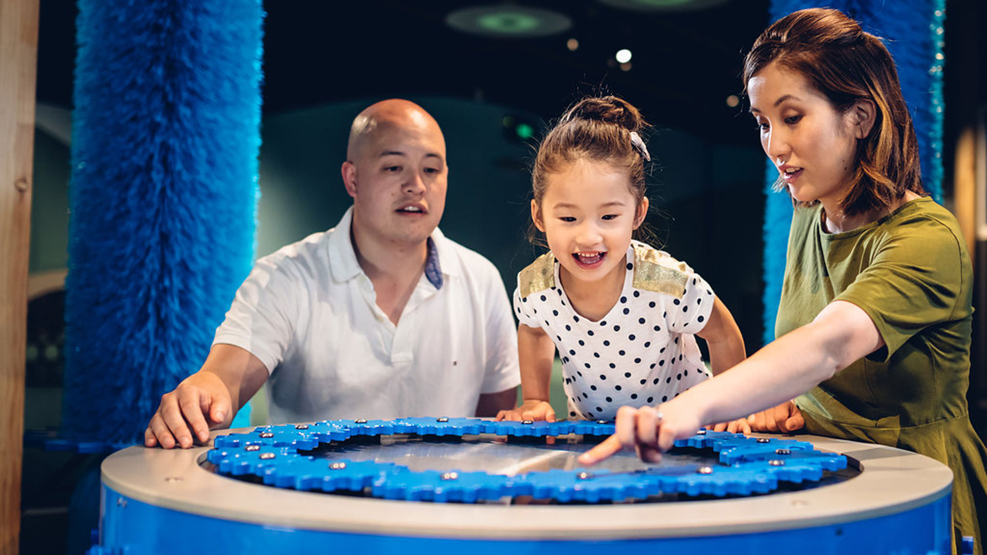 Child between a man and a woman using an exhibition interactive