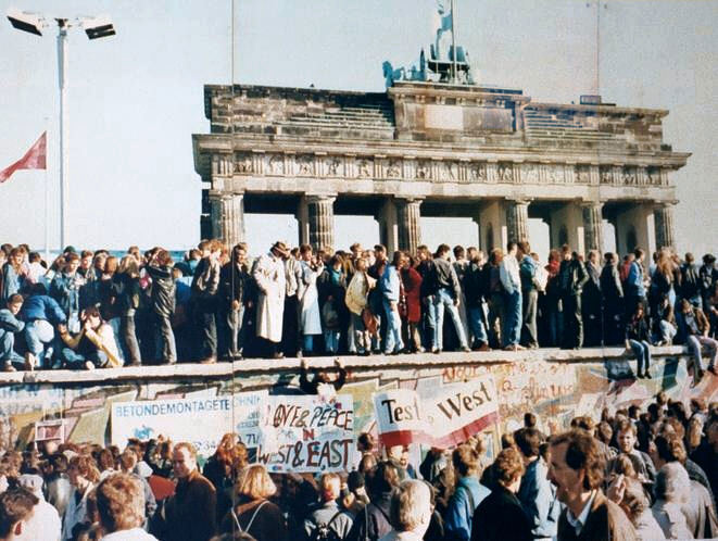 A crowd of people on top of a wall with a gate of stone columns behind them. 