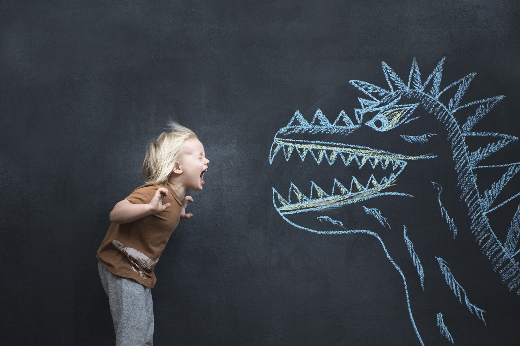 A boy yells at a chalk-drawn dinosaur on a blackboard.