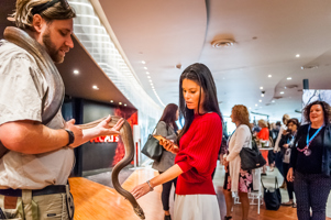 A python rest around a man's shoulders. A woman is holding out her hand to touch the animal