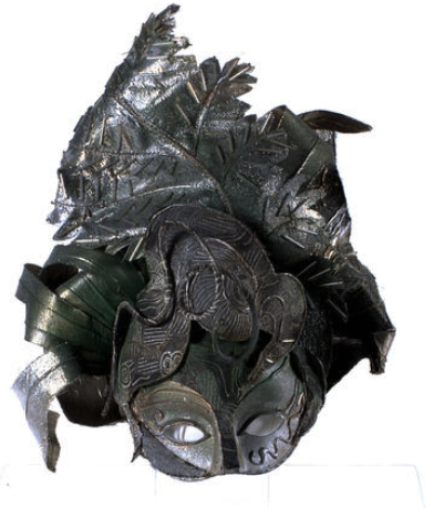 Face mask with decorative head piece made from fabric scraps in green and gold colourings.