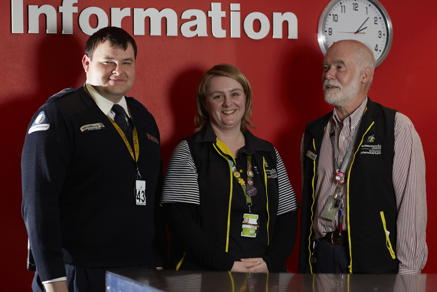 Two men and one women standing in front of sign