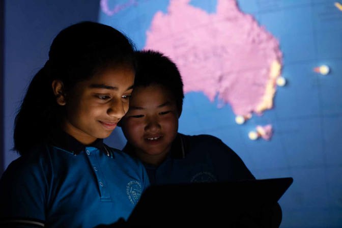 Two children looking a ipad. There is a large scale globe in background