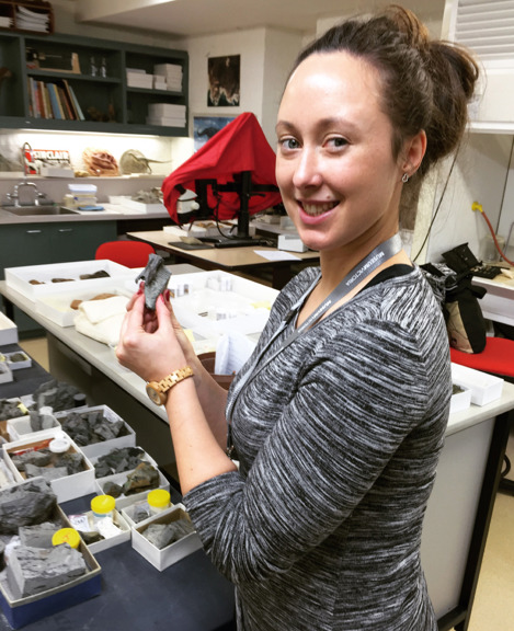 Woman, in a science laboratory holding a small fossil.