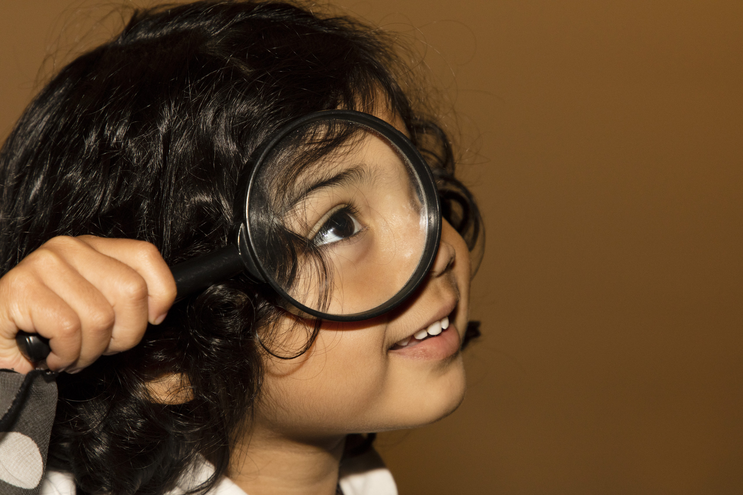 Child holding a magnifying glass up to their face