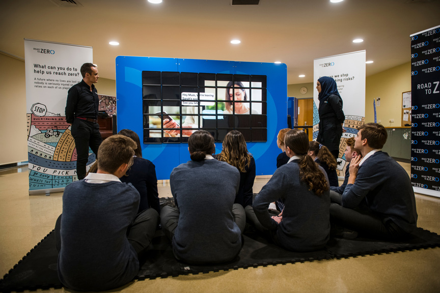 Several students seated in front of a screen flanked by Road to Zero presenters