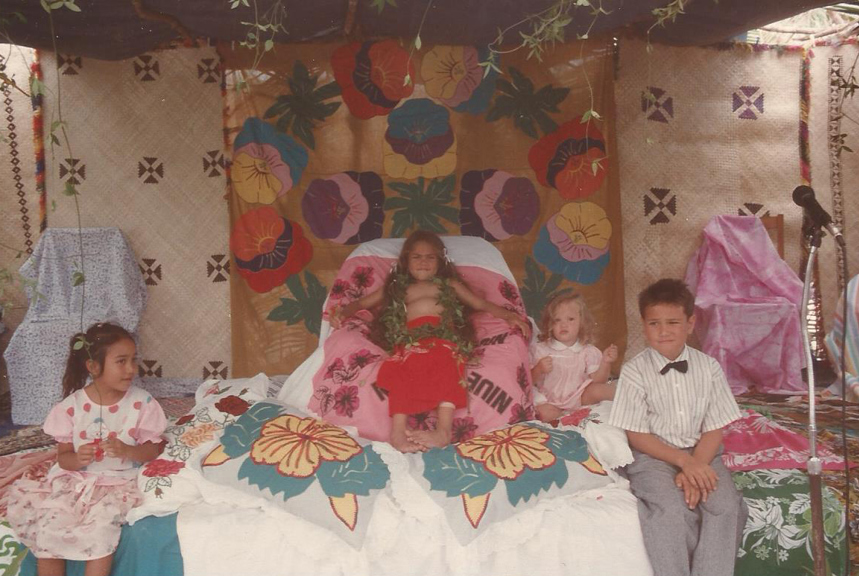 Four children sitting on platform. One is sitting on a ceremonial chair