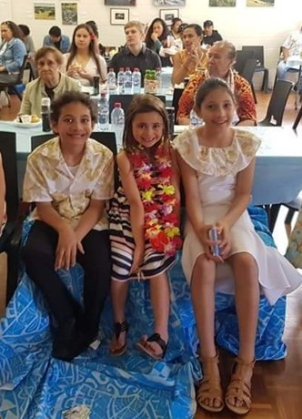 Three children sitting in front of a group of people