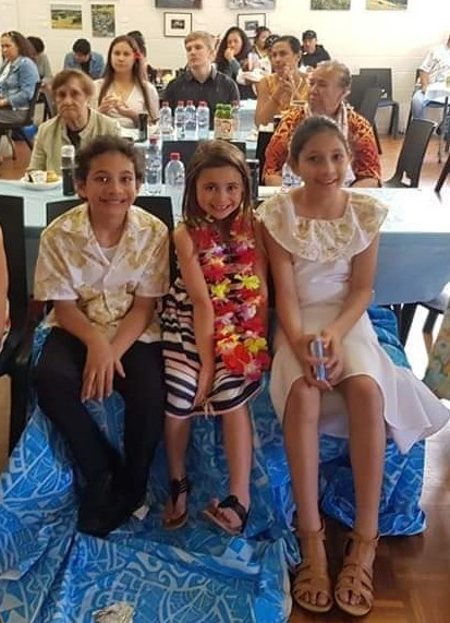 Three children sitting in front of a group of people