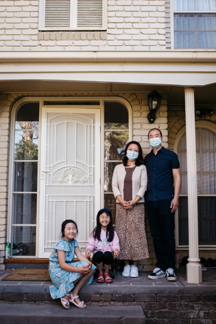Family of four posing at the front door. The adults are wearing face masks
