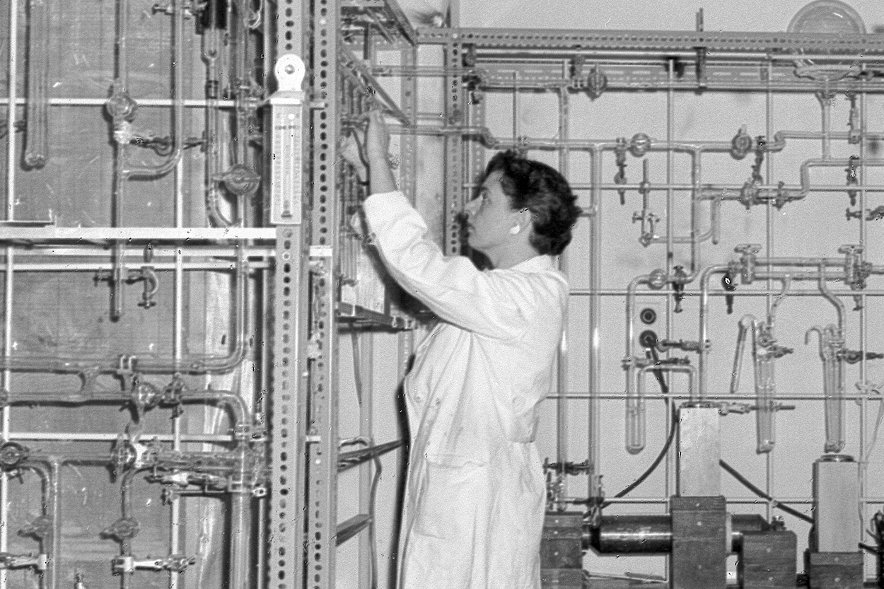 Black and white image of a woman wearing a lab coat in a science lab