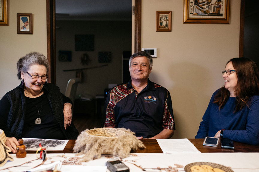 Three people sitting at a table. There are baskets, documents and a recording device on the table..