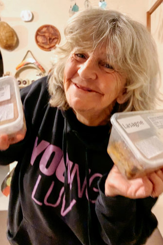 A woman is smiling and holding food containers