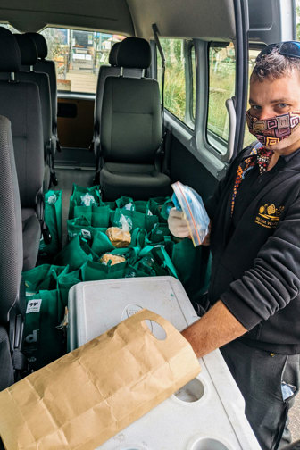 Man wearing a mask. He is standing at the door of van loaded with food deliveries.