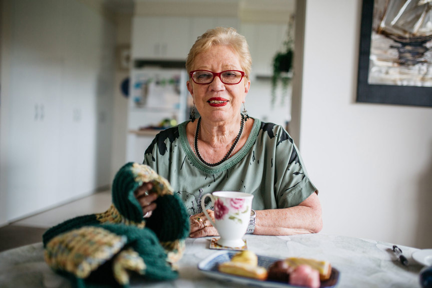 Woman sitting at table she is holding a knitted scarf and has a teacup in front of her