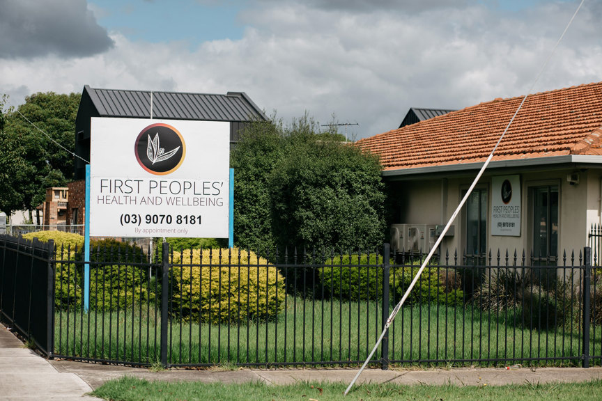 The outside of a building that is behind a black garden fence. There is a sign in the garden