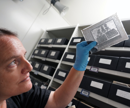 a woman holds a damaged black and white photo negative up to the light