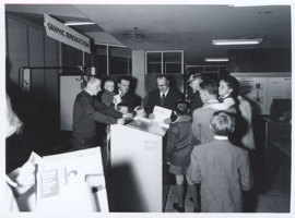 Group of men and young boys gathered around a piece of equipment in an exhibition display stand. 