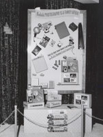 Exhibition display panel. The panel, set against a crushed velvet curtain, has products and signage suspended from it. A chain link barrier fence is visible in the foreground.