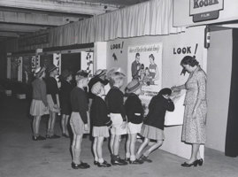 Two lines of children queuing to look through a view finder. A woman standing a the top of the line supervising. a the 