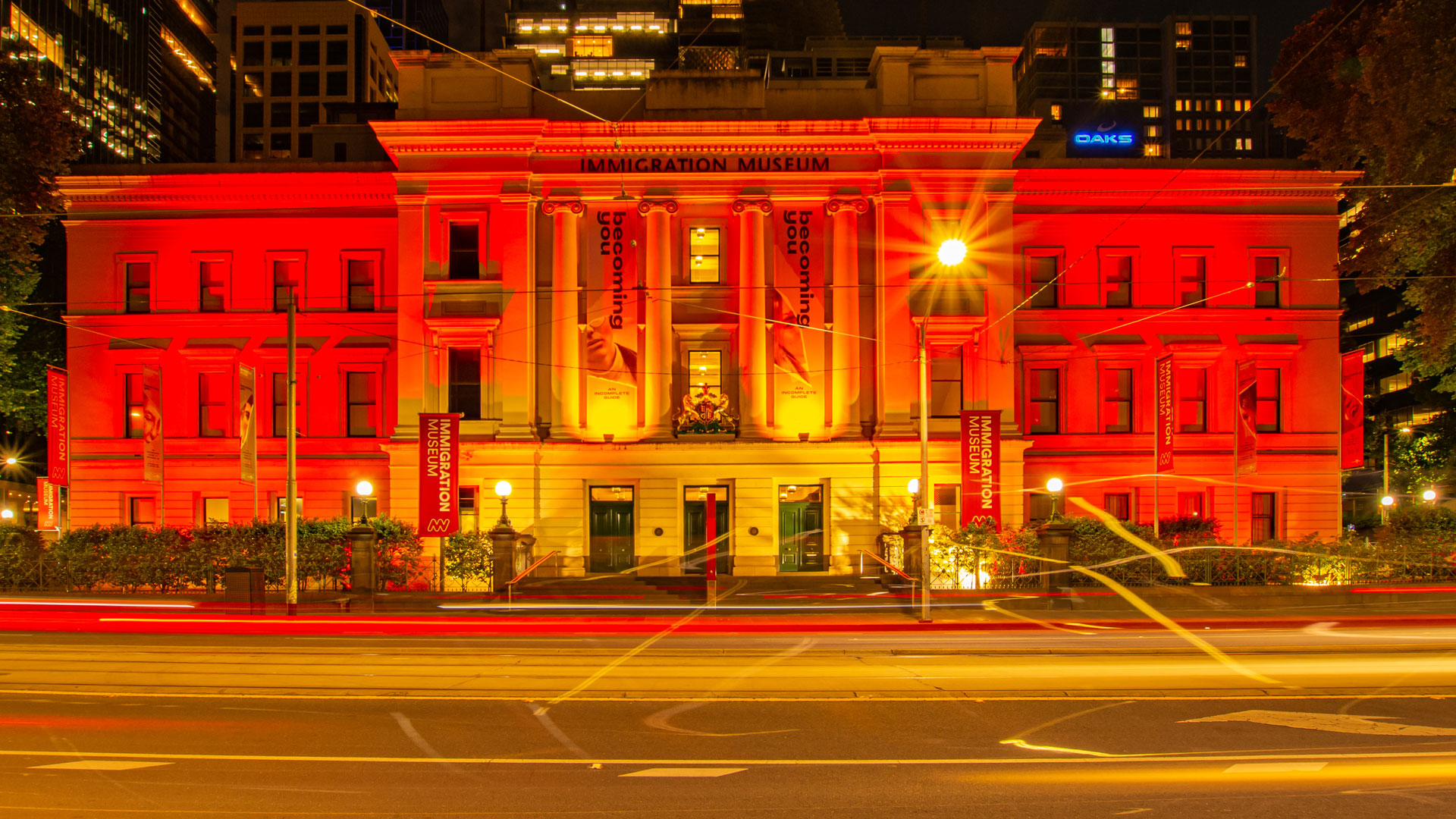 Immigration Museum at night lit up with red lights. Other buildings can be seen in the background