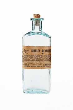 Glass bottle with cork stopper and paper label on the front with printed text in black ink. Bottle is empty of contents but there are some powdered residues on the cork.