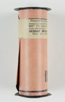 Black metal spool with cellulose nitrate film, sealed and covered in a protective pink paper cover and sealed with a printed Kodak sticker.