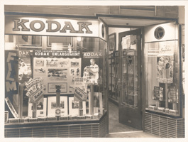 Entrance to shop with two display windows either side of door. Larger window contains photographs, posters and boxes of film.