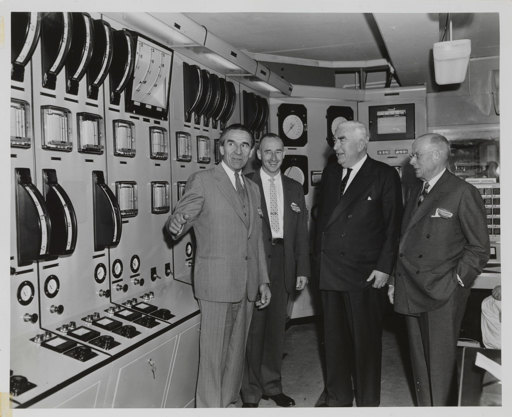 Four men in front of large control panels