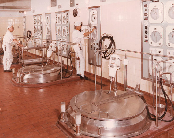 People in white coats in front of wall of controls 