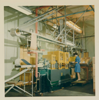 Woman wearing a blue dress and sandals operating a machine in a factory