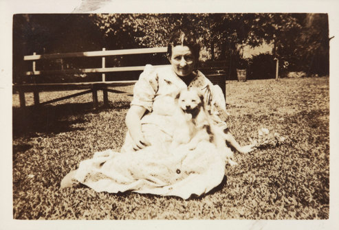 Woman seated on grass with small dog on lap.
