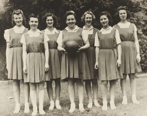 Seven women in sporting attire, one holding a basketball