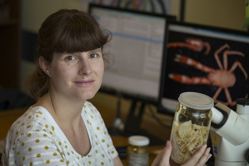 A photograph of a woman holding a jar containing dozens of small crustaceans 