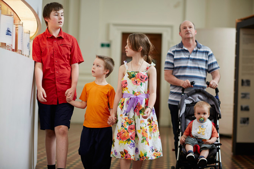Dad pushing pram and three children walking  in the Immigration Museum.