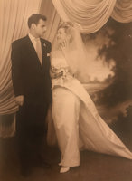 Man in suit with woman wearing tiara, veil, and dress with a train.