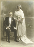 Woman in dress with train standing next to a seated man in suit.