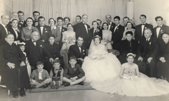 Bride and groom surrounded by people in formal setting.