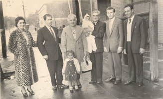 Six adults, one child and a baby  standing on a sidewalk