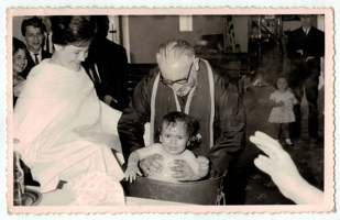 Woman watching priest immerse child in font.
