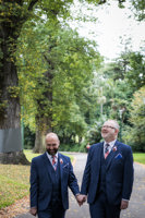 Two men in suits holding hands in park