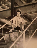 Woman standing on steps, holding suitcases.