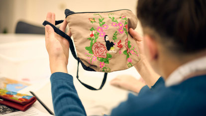 Back of head of a student holding and looking at a bag with embroidery on it, during an education program at the Immigration Museum.  