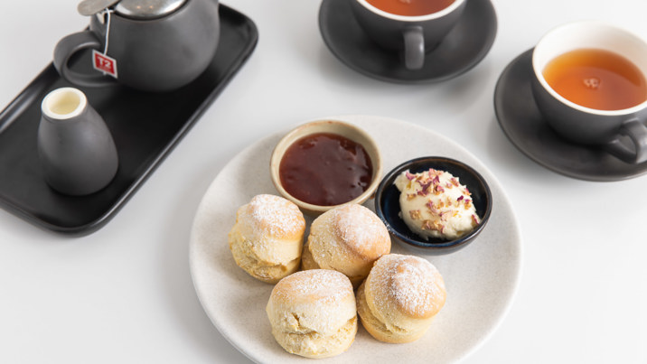 Two cups of tea served with freshly made scones, forest berry preserve jam and clotted cream.