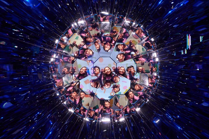 Faces and hands of young people reflected colourfully in countless facets of a disco ball