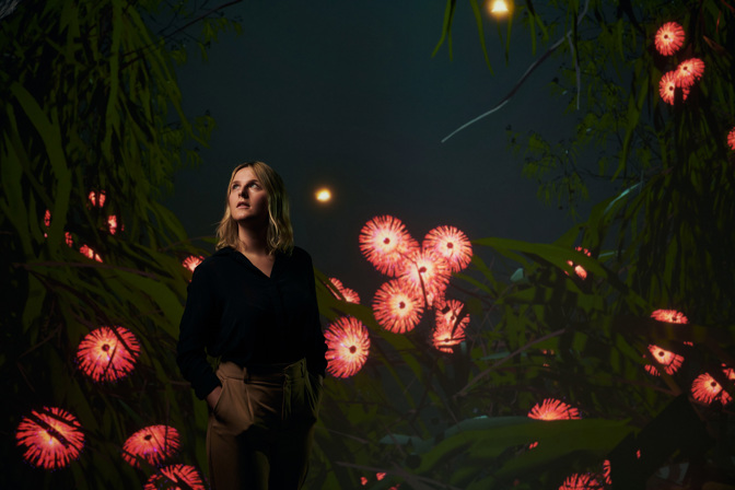 A woman surrounded by digital imagery suggesting a jungle with luminous blossoms