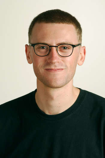 Head and upper torso of a bespectacled man in black