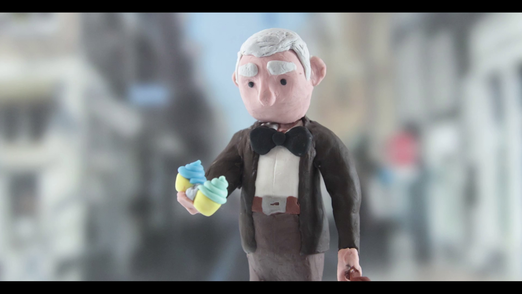 A clay figurine of an elderly man holding two cupcakes.