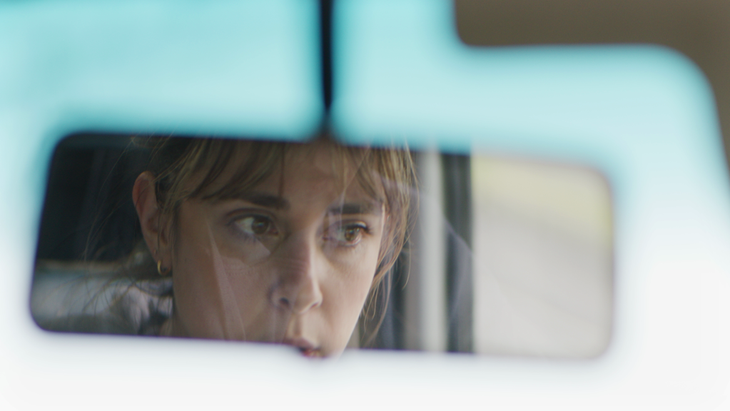 A reflection of a woman in the windscreen mirror of a car.